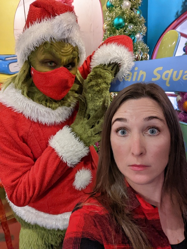A woman in black and red plaid shirt makes a silly face while the Grinch grumpily poses behind her at Universal Orlando.
