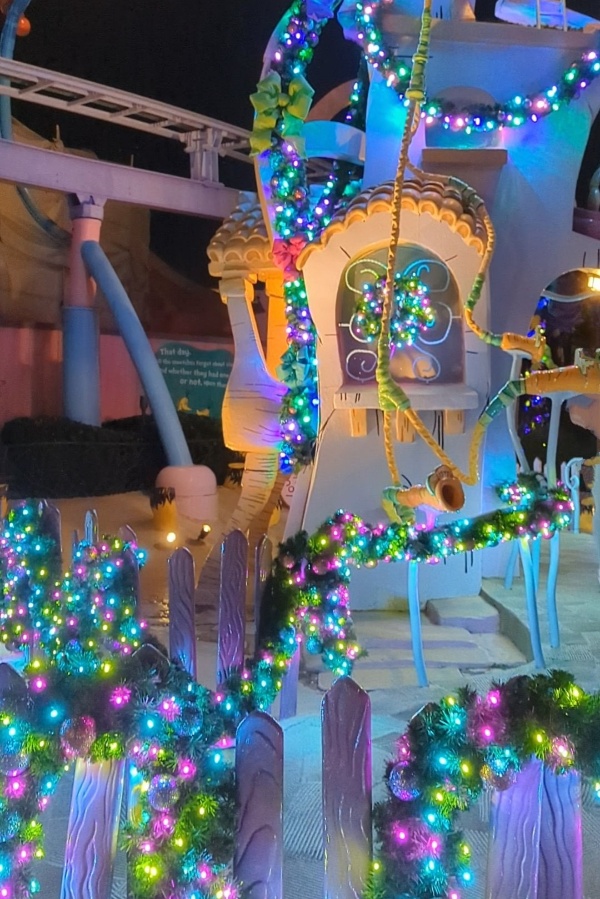 Pink, icy blue, and yellow lights wound through pine garland make Seuss Landing at Christmas sparkle 