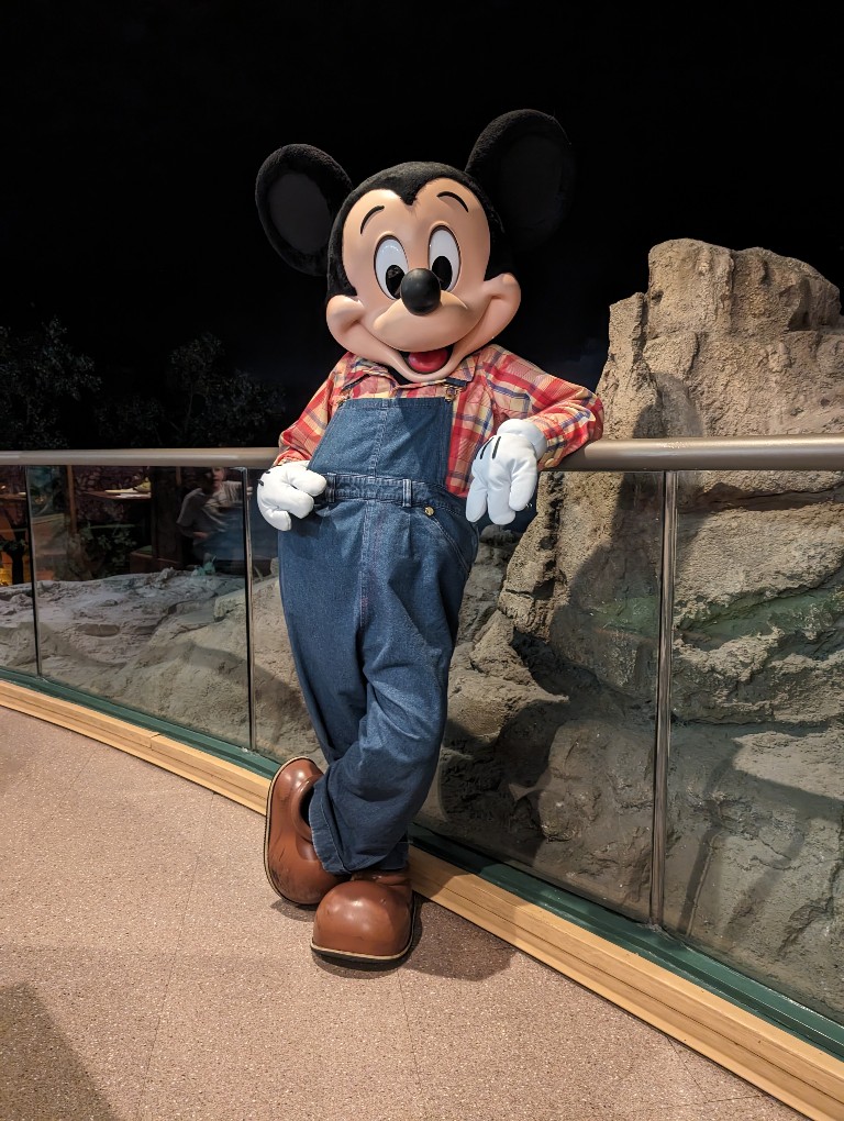 Farmer Mickey leans against a railing in jean overalls and a plaid shirt at Garden Grill