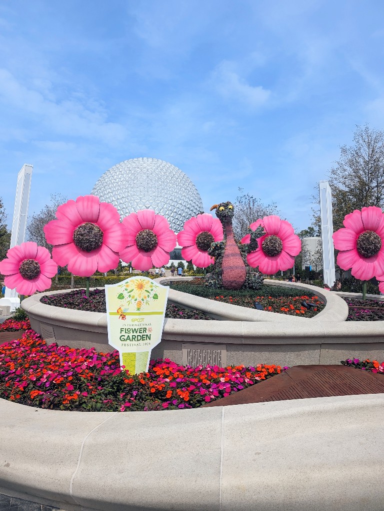 Figment topiary surrounded by large stylized pink flowers in front of Spaceship Earth