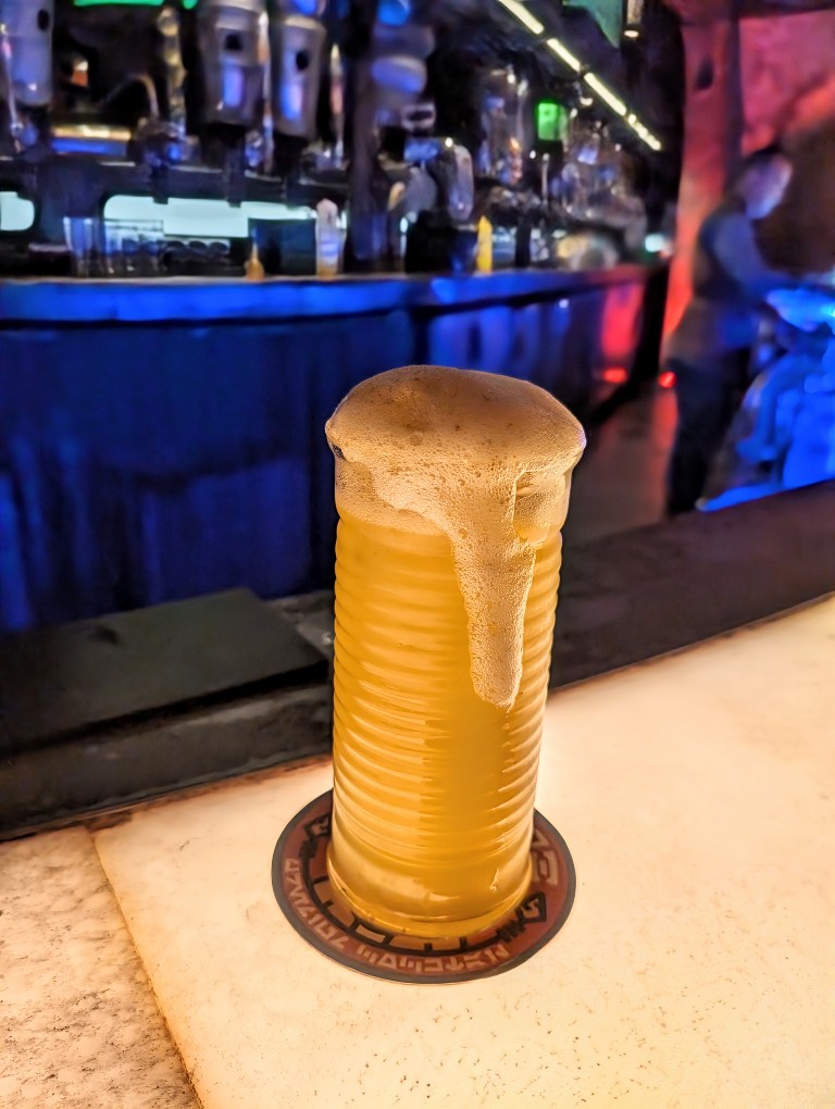 A orange drink covered in white foam in a tall glass sits on the Oga's Cantina bar