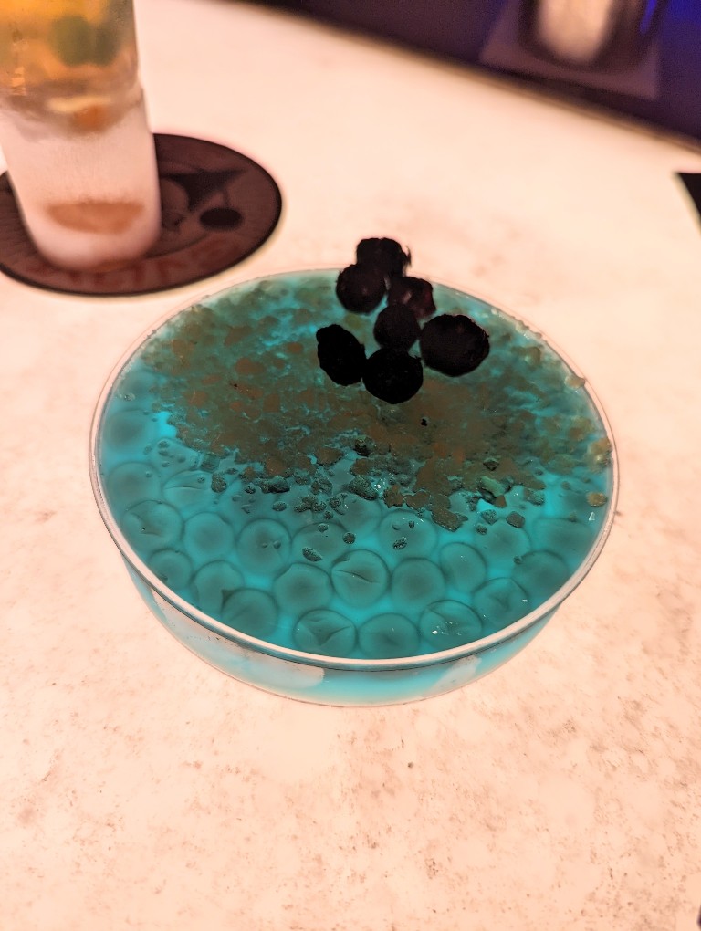 Oga's obsession is a non-alcoholic provision of blue lemondade jello layered with popping pearls and dried fruit served in a petri style dish at Oga's Cantina