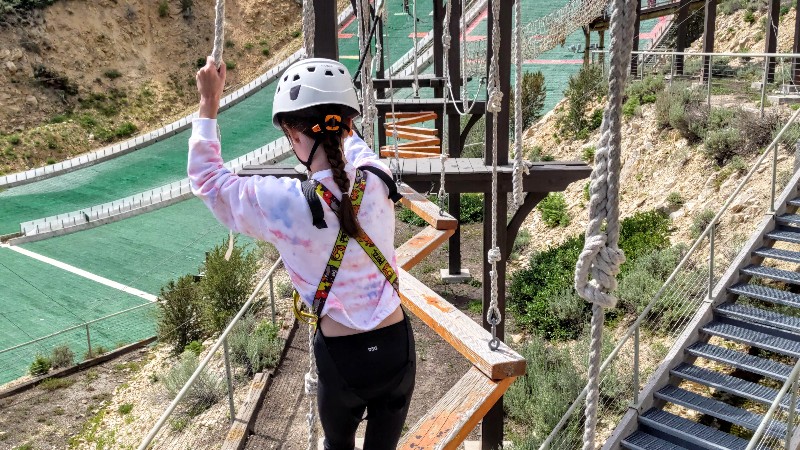 Girl in tie dye shirt walks across wooden planks on ropes course.