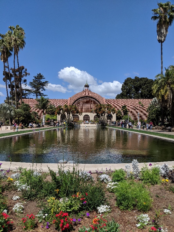 Balboa Park botanical building framed by blue skies above and a lily pond in front.