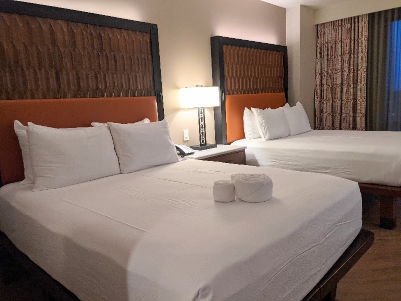 Two queen beds have wood-like headboards with a pop of orange and crisp white sheets at Gran Destino Tower.