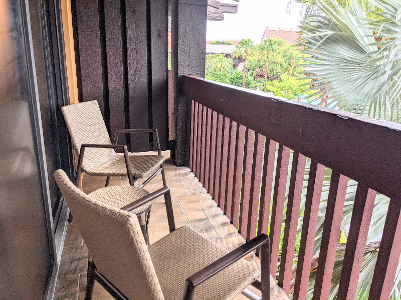 Two chairs on a private balcony surrounded by a palm tree.