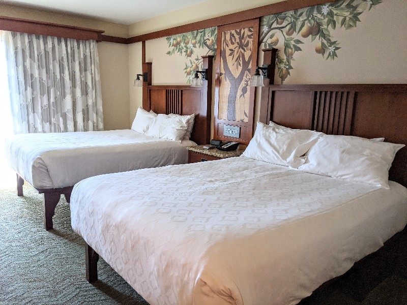 Crisp white linens on two queen beds with and orange tree mural adorning the wall behind.