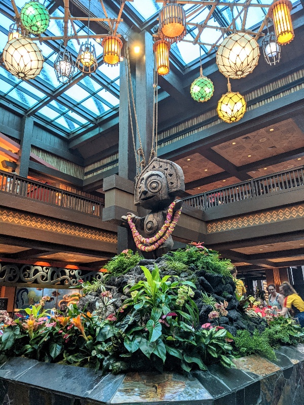 Carved wood figure surrounded by hanging lanterns and lush plants in the Polynesian Resort lobby.