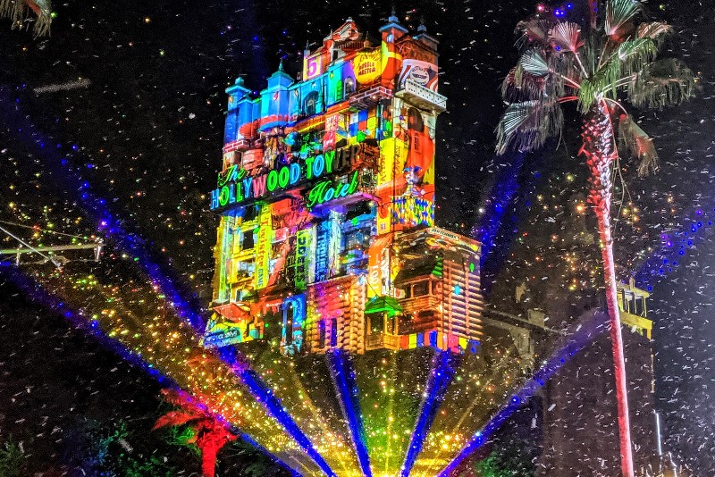 Faux snow falls in Hollywood Studios with Sunset Seasons Greetings projections on the Tower of Terror during Disney World Christmas