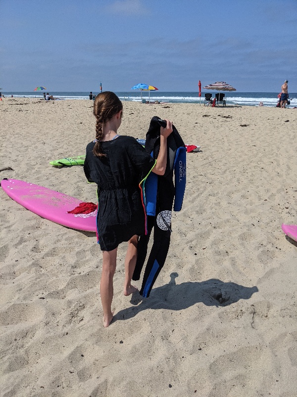 Girl holds wetsuit as she prepares for Pacific Surf School lesson