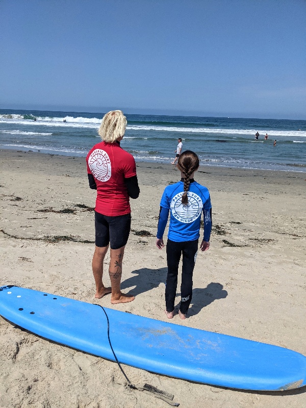 Pacific Surf School instructor looks out over the water with a student by his side.