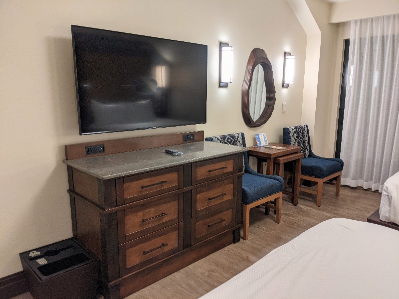Medium size dresser, wall mounted TV, and two blue side chairs with table at Disney's Wilderness Lodge