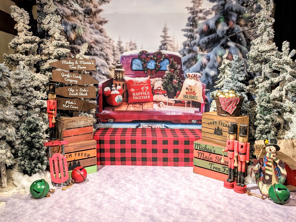 Flocked pine trees surround what looks like the bed of an antique pick up truck for a holiday portrait at Disney Springs PhotoPass Studio