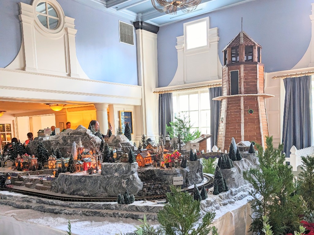 A detailed miniature train goes through several different Disney scenes with a towering gingerbread lighthouse in the background