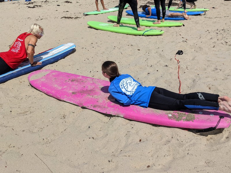 Girl listens intently to Pacific Surf School instructor on how to properly stand on surfboard