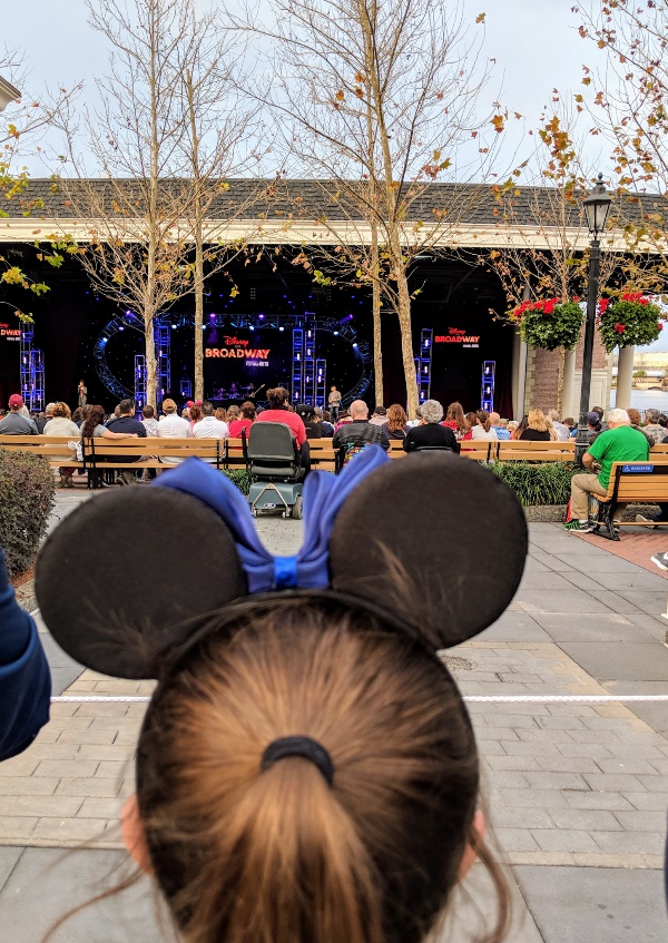 Girl stands behind a crowd to listen to Disney On Broadway during Epcot Festival of the Arts