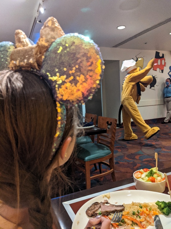 Girl in sequin ears looks across Chef Mickey's at Pluto waving to another table