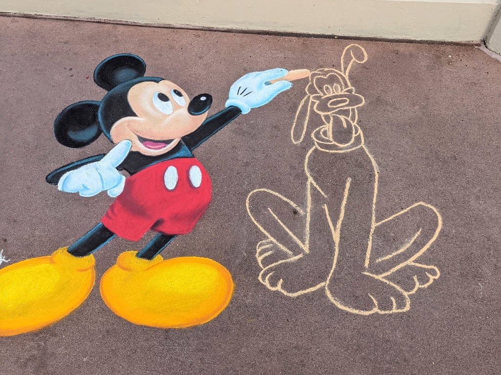 Chalk art piece of realistic Mickey Mouse drawing Pluto in chalk
