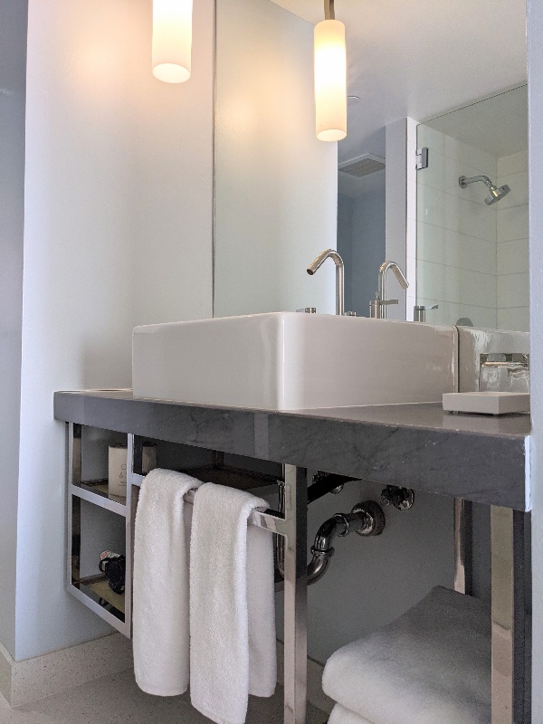 A mix of white tiled shower and industrial gray counters in the Tower 23 ocean view room bathroom