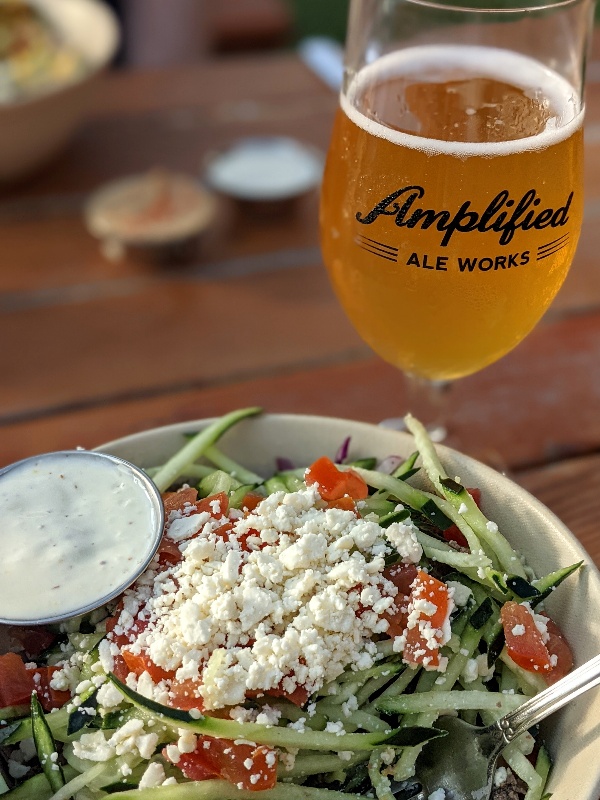 A glass of beer next to a Mediterranean style dinner at Amplified Ale in Pacific Beach