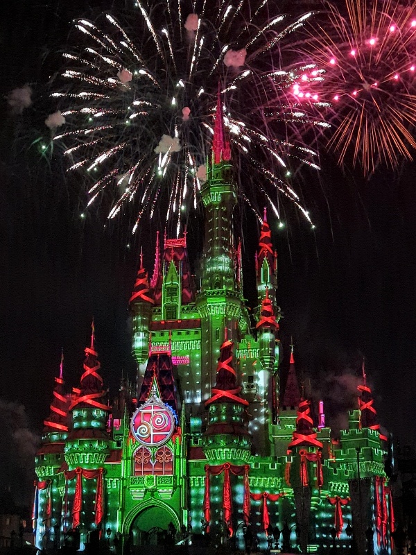 Cinderella castle in green and red lights with fireworks overhead at Disney Very Merriest After Hours