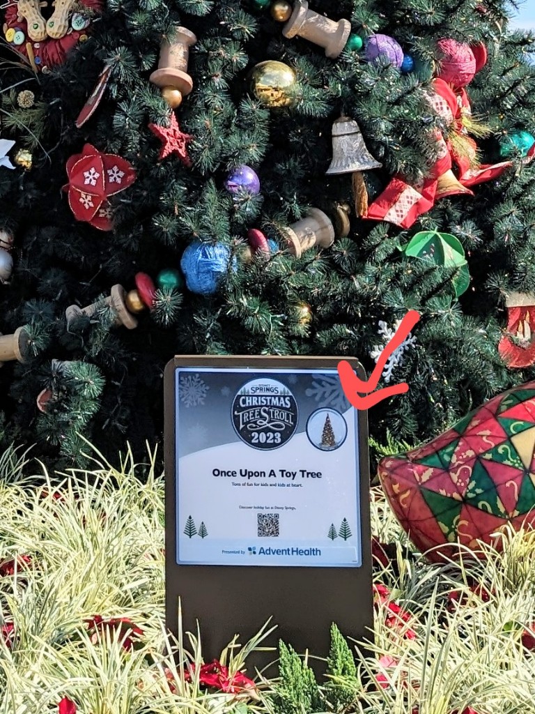 Sign for Once Upon a Toy tree with a red arrow pointing to the correct sticker for the tree on the Disney Springs Christmas Tree Stroll map