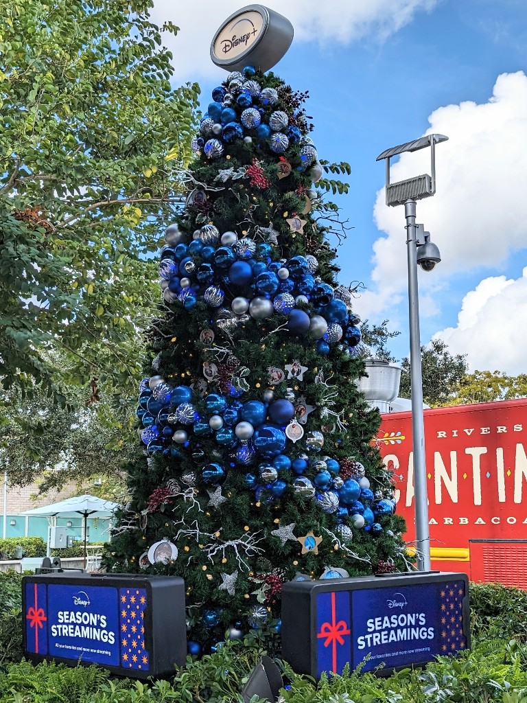 A garland of shiny ornaments in shades of blue ring the Disney Plus tree