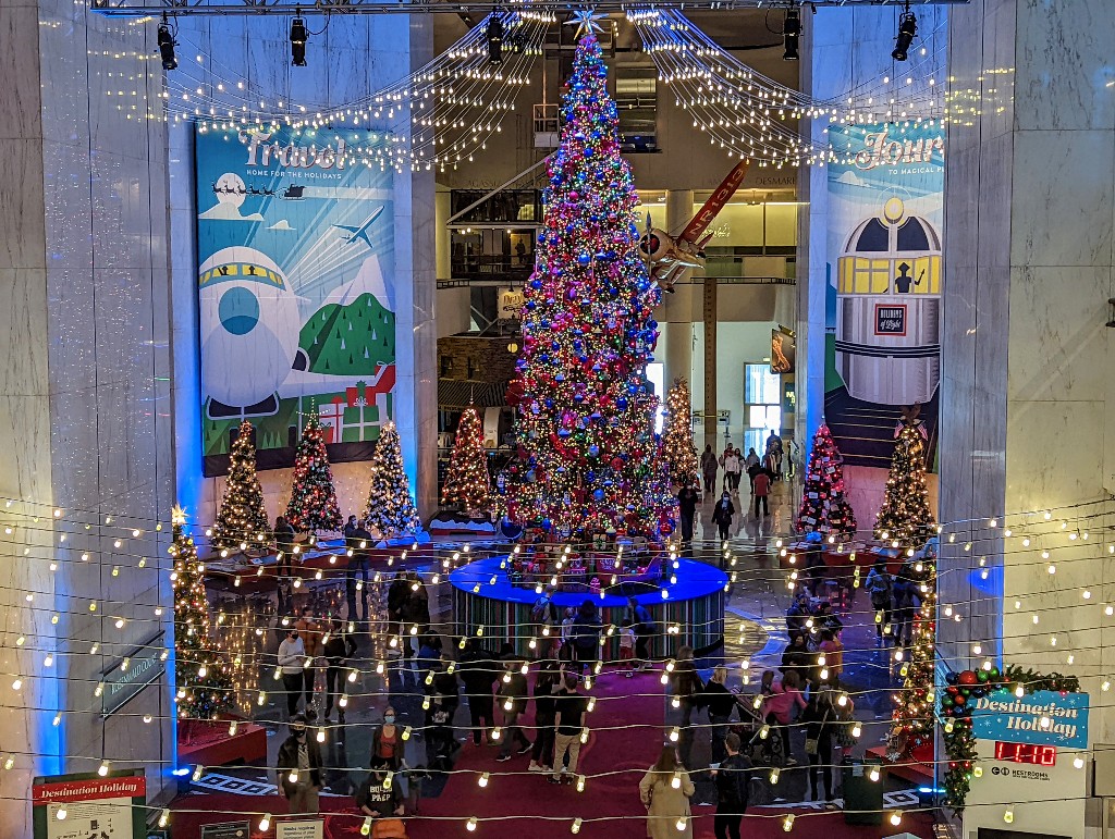 Multistory Grand Christmas Tree surrounded by several country inspired Christmas trees at Museum of Science and Industry