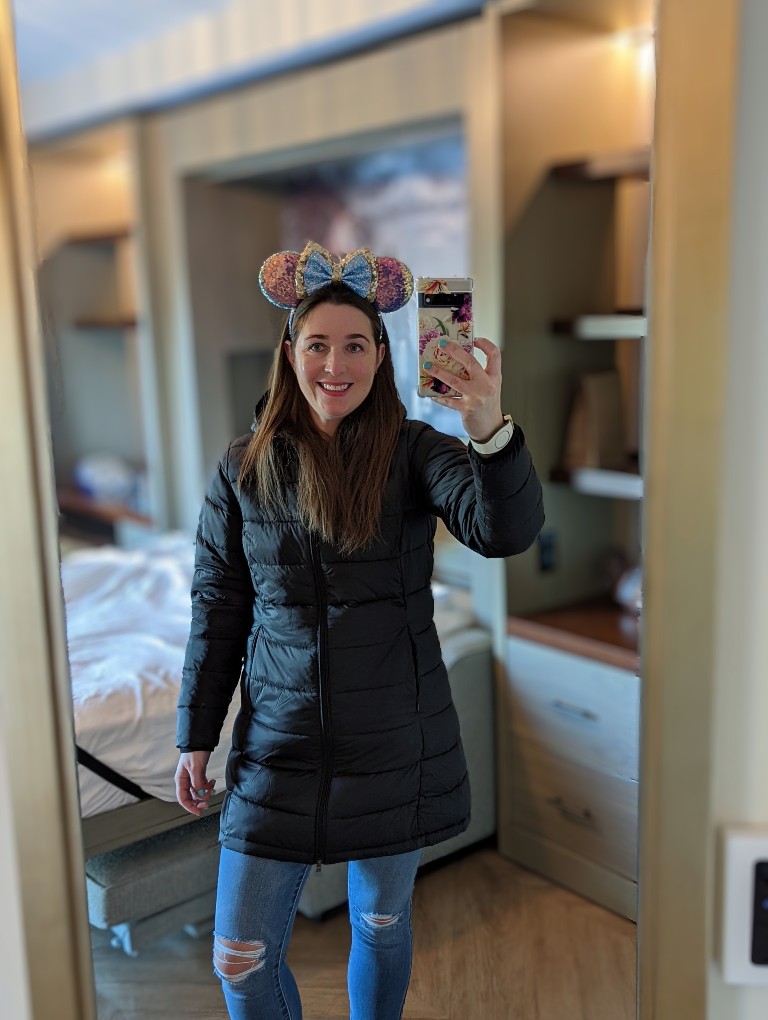 Woman takes a selfie wearing a packable down jacket and Minnie Mouse ears at Disney World