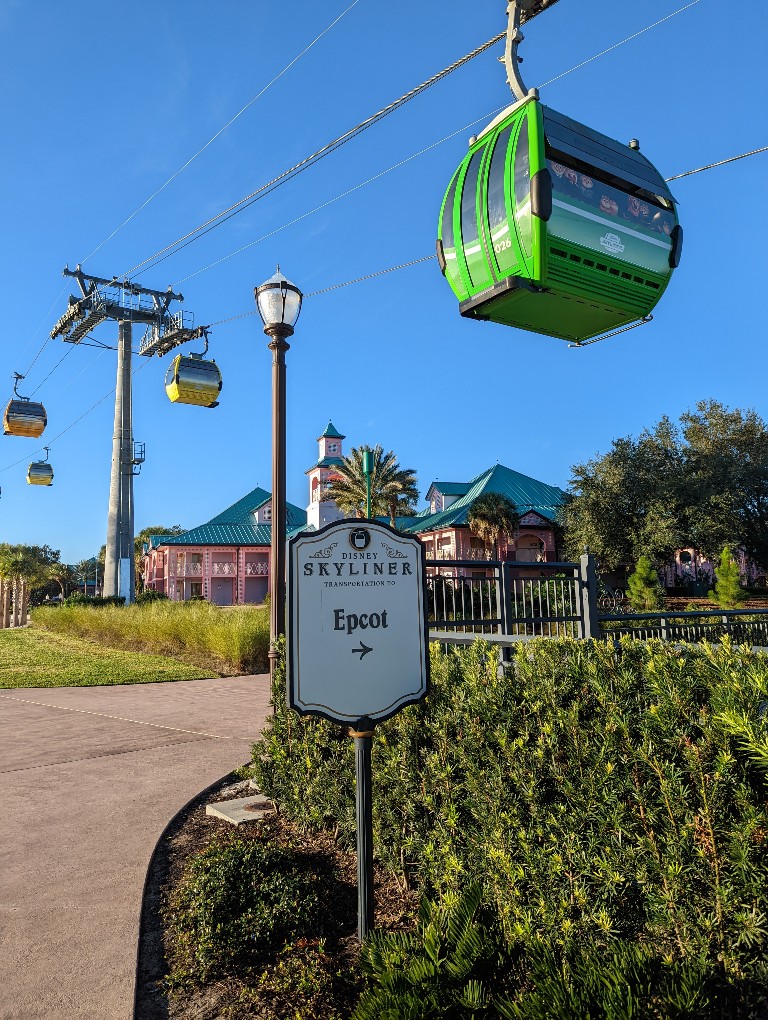 Green Disney Skyliner gondola hangs above a sign for Epcot