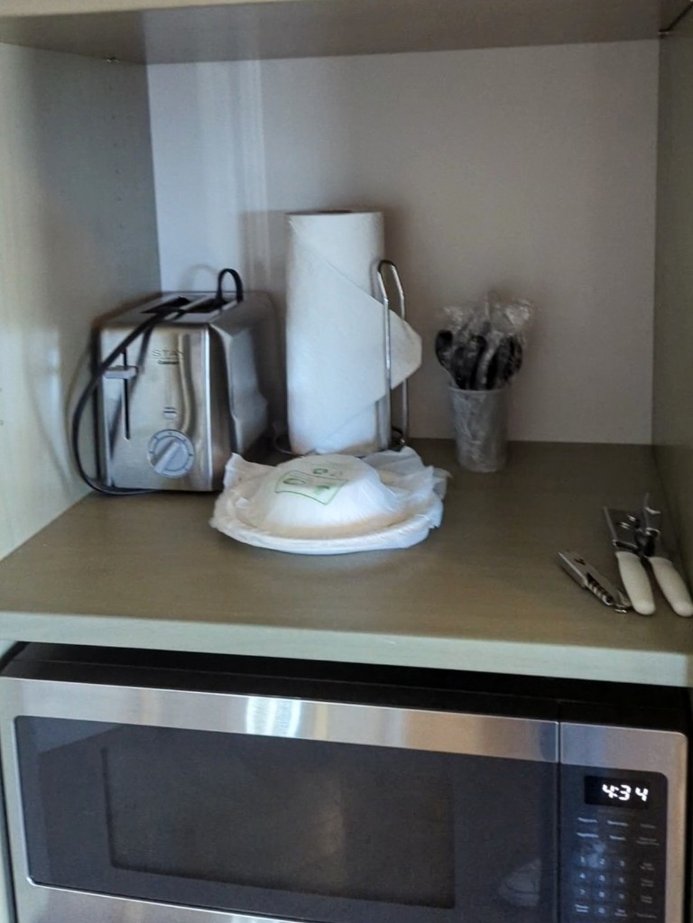 Paper plates, utensils, a toaster, and paper towels inside a cabinet in a Riviera Resort Tower Studio