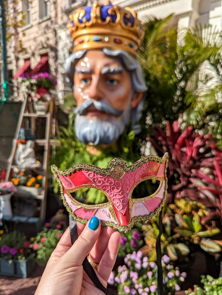 A glittering, pink Mardi Gras mask prize is held in front of a large Universal Mardi Gras photo op