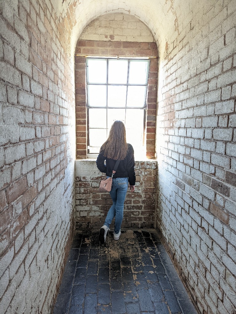 Girl looks out a brightly illuminated window with whitewashed brick on either side at Tybee Island Lighthouse