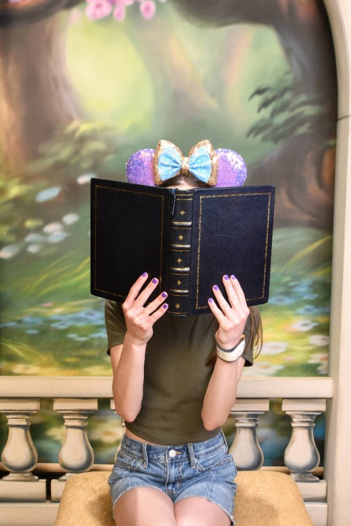 Girl poses with Mickey ears behind a book