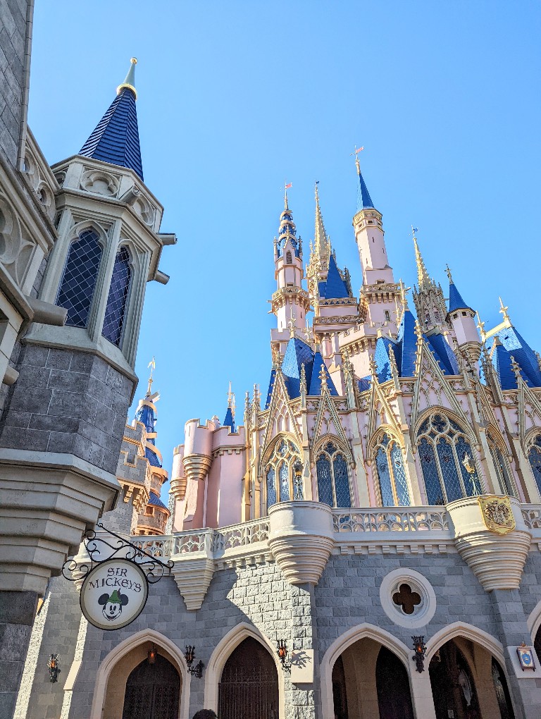 A round Sir Mickey's sign hangs on a building behind Cinderella Castle