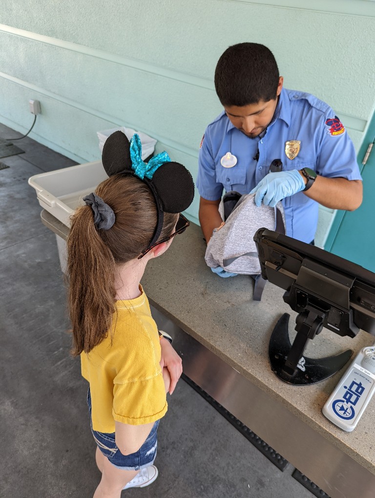 A girl waits as Disney World security guard looks through her backpack