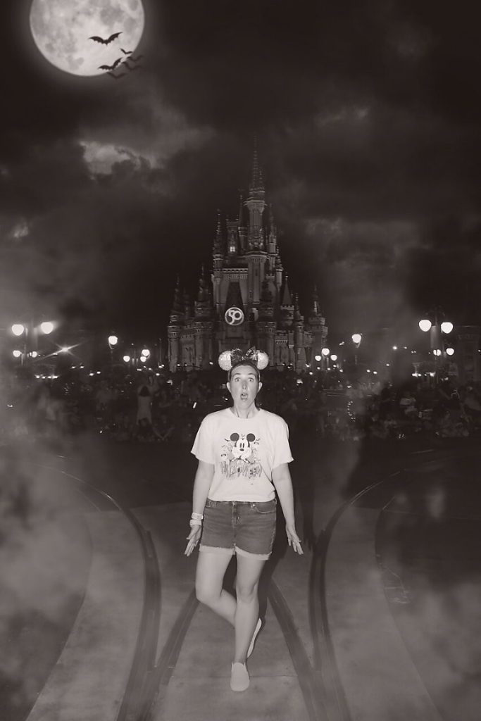 A woman looks frightened in a black and white MNSHHP Magic Shot with a large moon, bats, and Cinderella Castle in the background