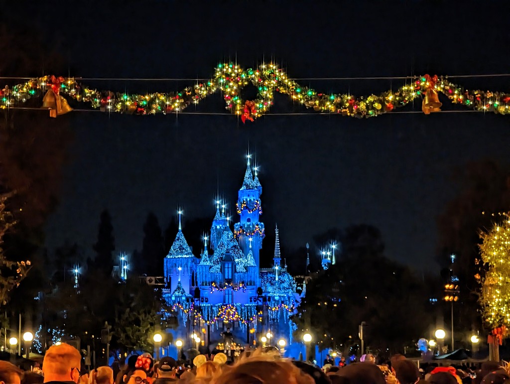A lighted, decorated Mickey wreath and garland hang above Main Street in front of Sleeping Beauty Castle