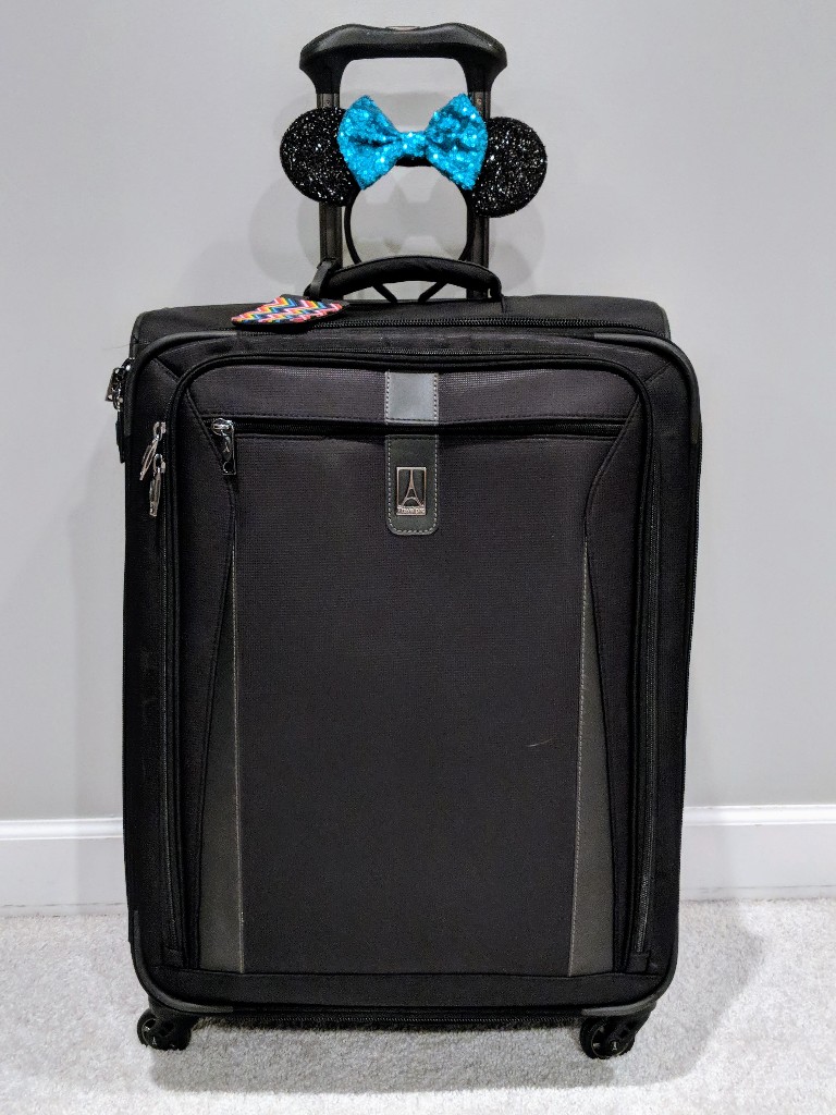 Minnie Mouse ears with a teal bow perched on top of a large black suitcase