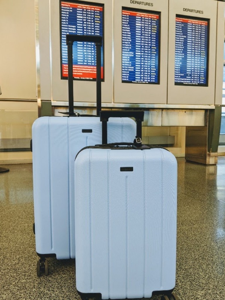 Two sky blue suitcases sit in front of a airport departure board
