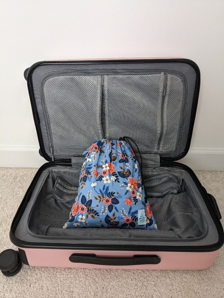 A floral print, waterproof bag sits inside a pink carry on suitcase