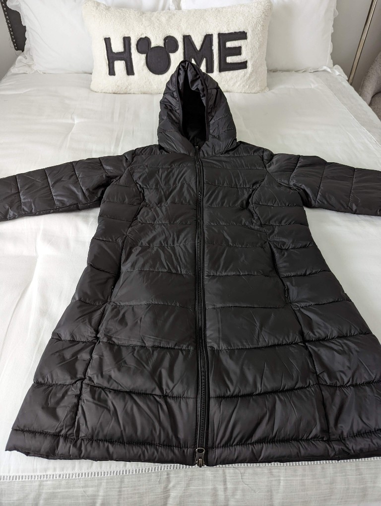 A packable down jacket sits on top of a bed with Disney themed pillow behind