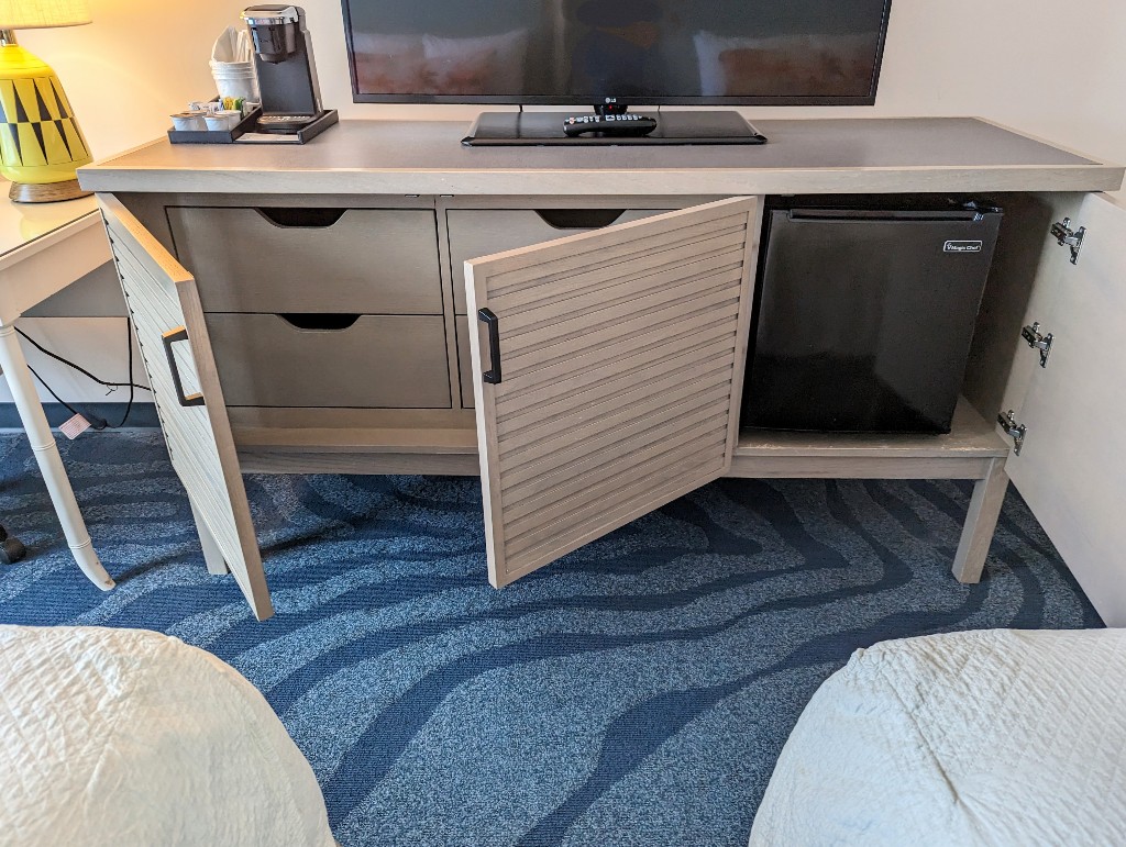 A cabinet holds the TV and coffee maker while the doors below conceal drawers and a mini fridge at Sapphire Falls Universal Orlando