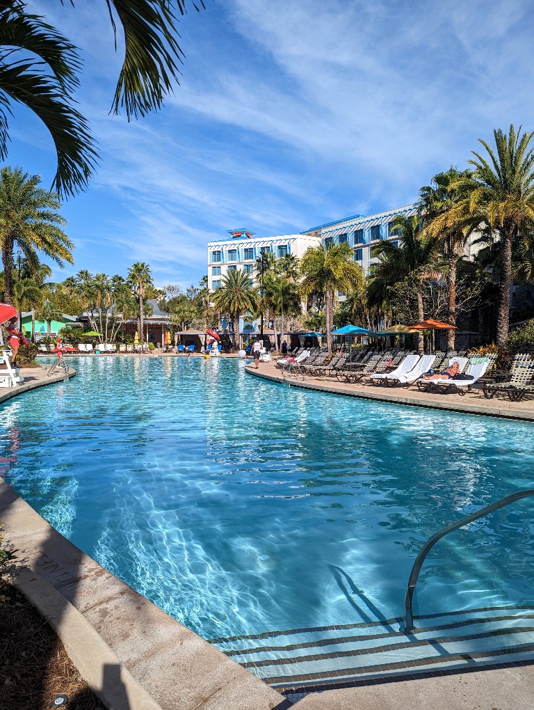 Blue skies with wispy clouds reflect in a turquoise pool framed in palm trees and surrounded by sand at Sapphire Falls Resort