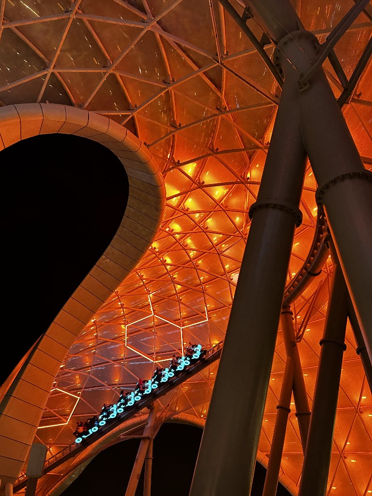 Tron Lightcycles zoom on the track under a brightly lit orange canopy