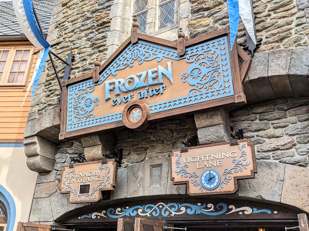 A carved sign hangs above the entrance to Frozen Ever After with a posted standby wait of 65 minutes and a Disney World Genie Plus Lightning Lane 2pm return time