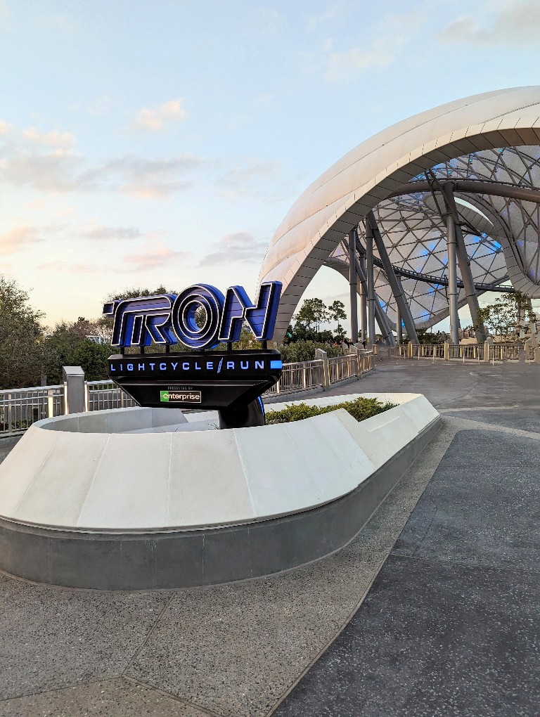 A bright blue Tron Lightcycle Run attraction sign in front of a large, curved canopy