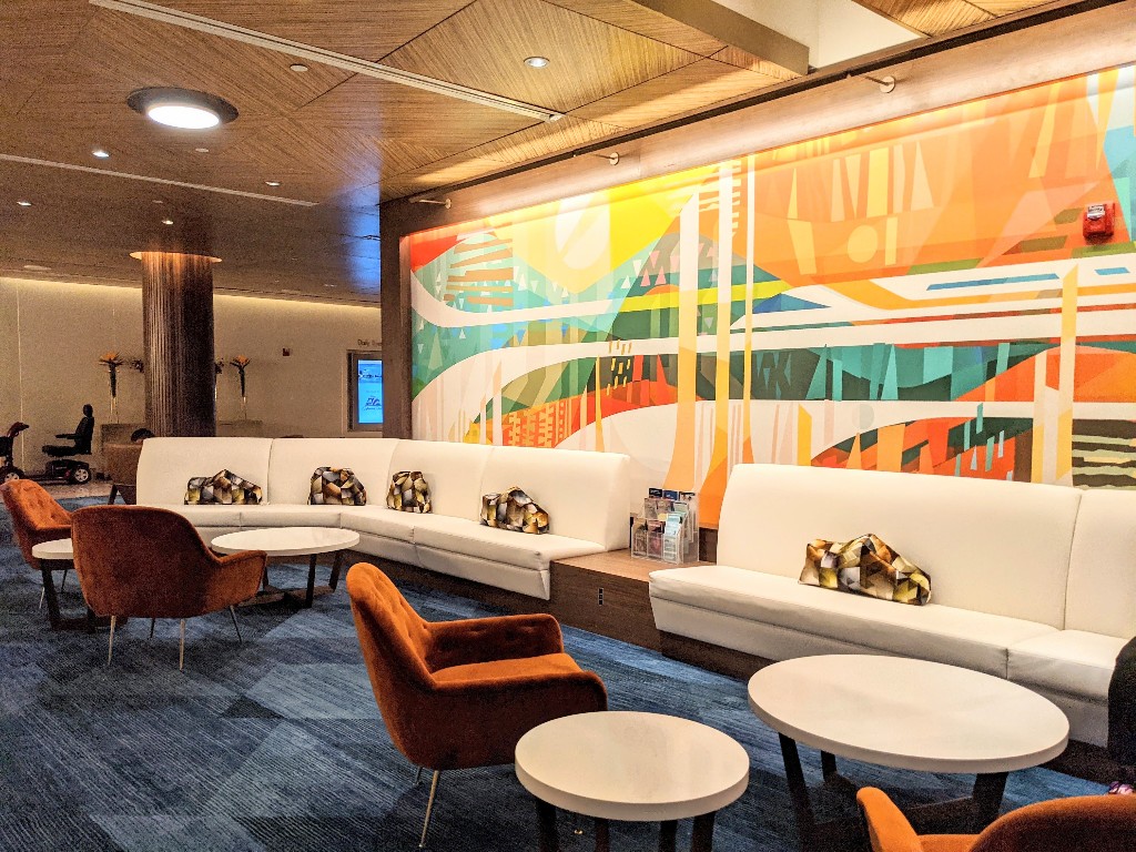 A bright mural in front of a sleek, long white couch, oval accent tables, and rust colored chairs provide an updated mid-century modern aesthetic to Disney's Contemporary Resort's lobby