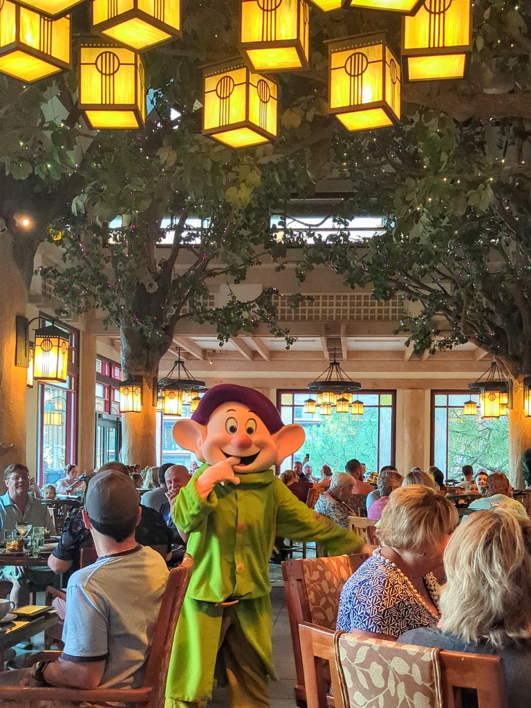 Dopey roams through Artist Point under leafy branches and shimmering lanterns