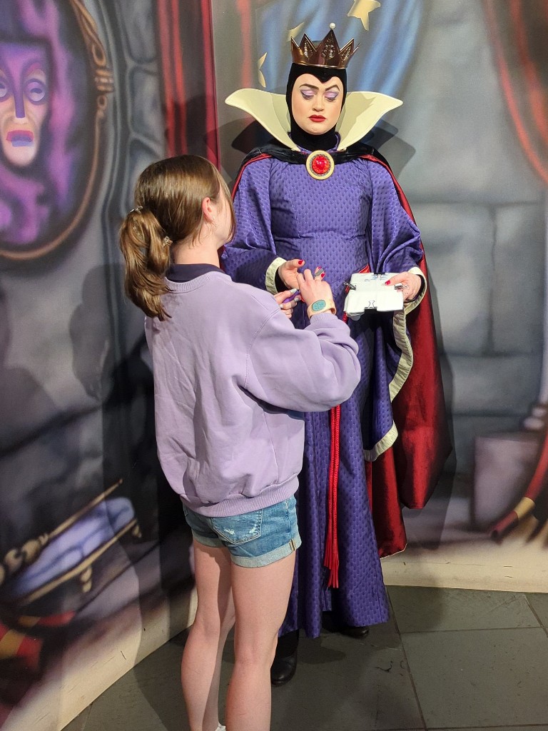 The Evil Queen grimaces in disgust while taking a marker to sign our Disney character autograph pillowcase
